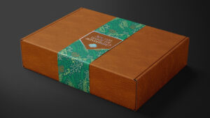 A wood-patterned cardboard mailer box wrapped with a floral belly band. The belly band is sealed with a sticker that reads, "Are you ready for adventure?" above the Girl Scout trefoil symbol.